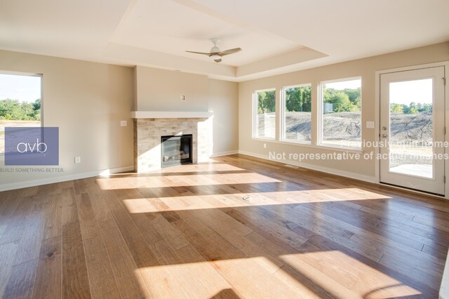 unfurnished living room with ceiling fan, a tray ceiling, and light hardwood / wood-style flooring