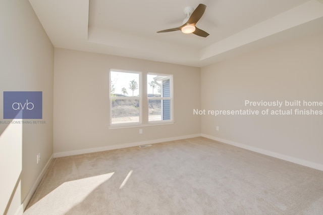 carpeted empty room featuring a tray ceiling and ceiling fan