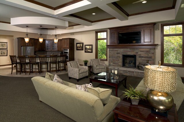 carpeted living room featuring coffered ceiling, a stone fireplace, ornamental molding, and beamed ceiling