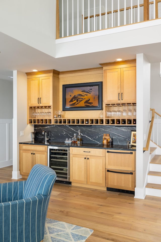 bar with wine cooler, a towering ceiling, light hardwood / wood-style flooring, and light brown cabinets