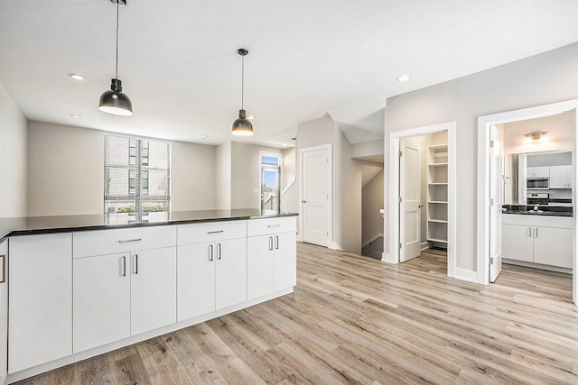 kitchen featuring light wood-type flooring, white cabinets, sink, and decorative light fixtures