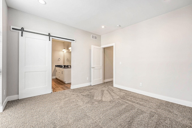 unfurnished bedroom featuring a barn door, connected bathroom, and light carpet