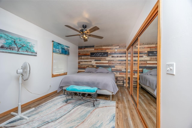 bedroom featuring hardwood / wood-style flooring, a closet, ceiling fan, and wood walls