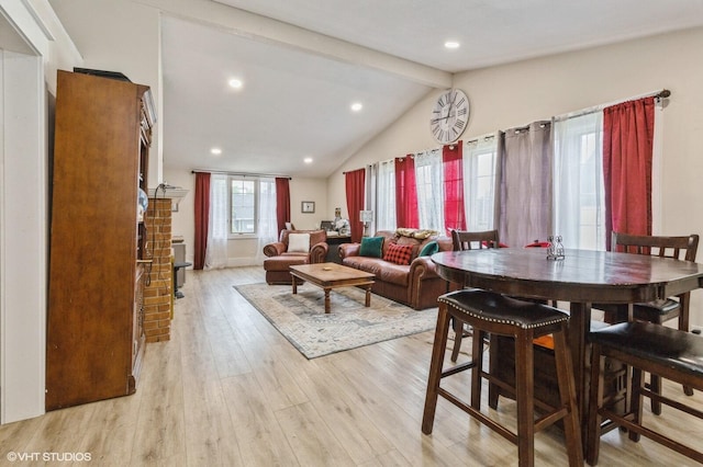 dining space with a brick fireplace, vaulted ceiling with beams, and light hardwood / wood-style flooring