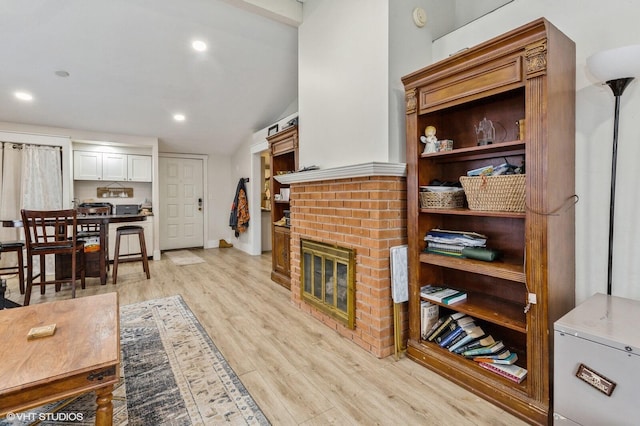 living room featuring vaulted ceiling, light hardwood / wood-style floors, and a brick fireplace