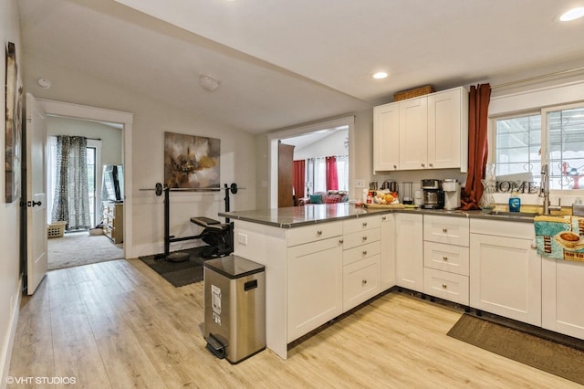 kitchen featuring lofted ceiling, sink, white cabinetry, kitchen peninsula, and light wood-type flooring