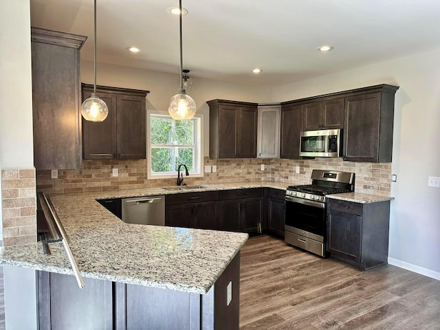 kitchen featuring sink, decorative light fixtures, light stone counters, kitchen peninsula, and stainless steel appliances