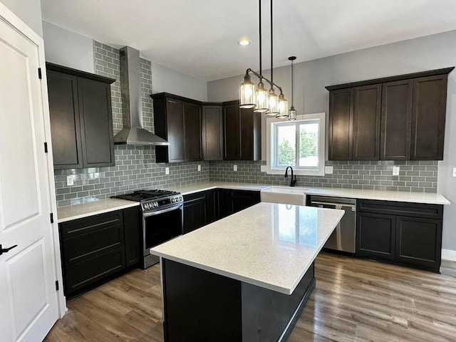 kitchen featuring sink, wall chimney exhaust hood, stainless steel appliances, pendant lighting, and a kitchen island