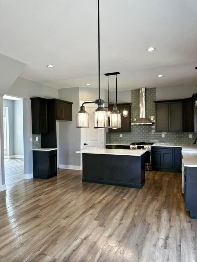 kitchen with gas range, a center island, wall chimney exhaust hood, hanging light fixtures, and hardwood / wood-style floors