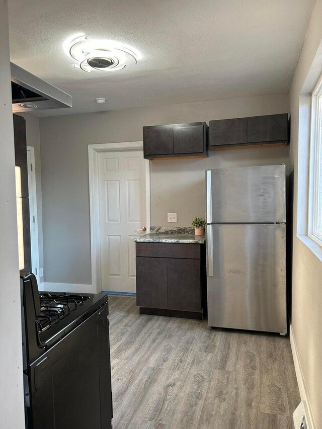 kitchen with light wood-type flooring, dark brown cabinetry, stainless steel refrigerator, and black range