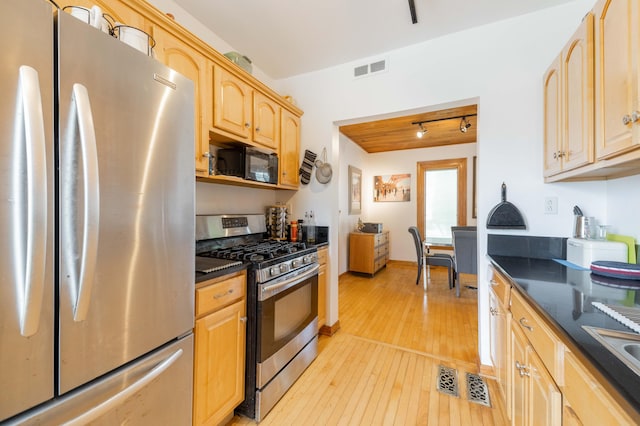 kitchen with light brown cabinets, light hardwood / wood-style flooring, dark stone countertops, and stainless steel appliances