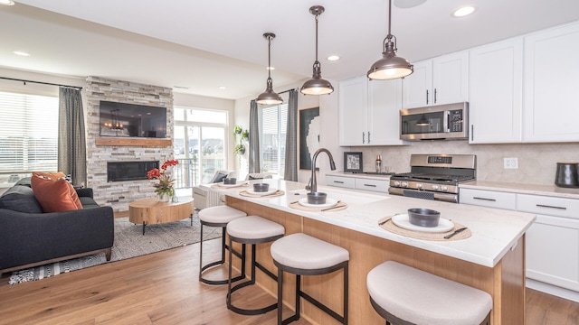 kitchen featuring white cabinetry, appliances with stainless steel finishes, hanging light fixtures, and a center island with sink