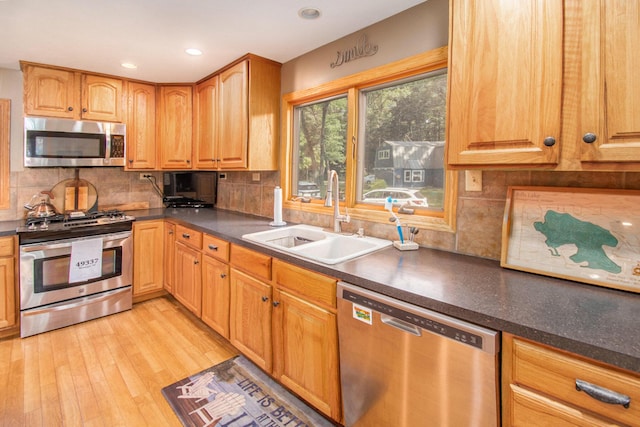 kitchen with appliances with stainless steel finishes, sink, backsplash, and light hardwood / wood-style flooring