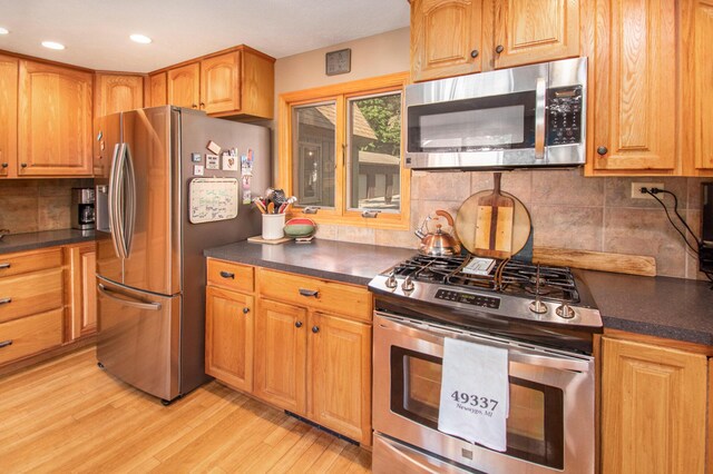 kitchen with appliances with stainless steel finishes, light hardwood / wood-style flooring, and backsplash