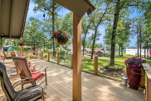 wooden terrace featuring a water view and a lawn