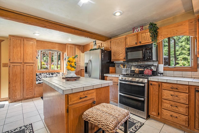 kitchen featuring light tile patterned flooring, a center island, tile counters, stainless steel appliances, and beam ceiling