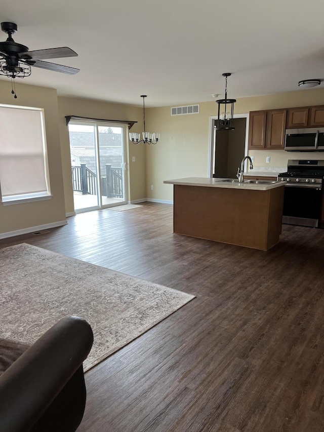 kitchen featuring a kitchen island with sink, hanging light fixtures, sink, appliances with stainless steel finishes, and dark hardwood / wood-style flooring