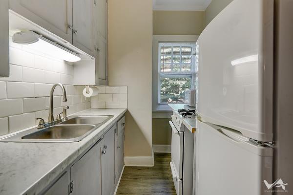 kitchen with decorative backsplash, white appliances, dark wood-type flooring, and sink