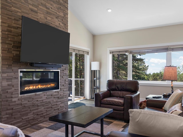 living room with a stone fireplace, vaulted ceiling, and light hardwood / wood-style flooring