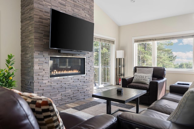 living room featuring a stone fireplace, vaulted ceiling, and light hardwood / wood-style flooring