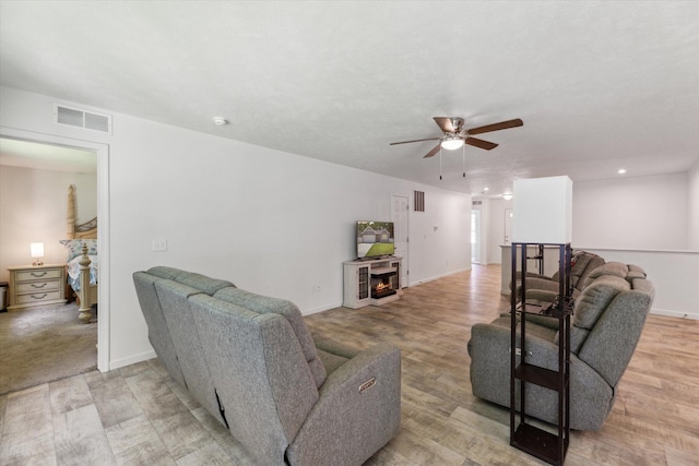 living room featuring ceiling fan, a fireplace, and light wood-type flooring