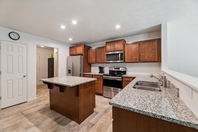 kitchen with light stone countertops, appliances with stainless steel finishes, a breakfast bar, sink, and a center island