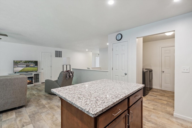 kitchen with a center island, light hardwood / wood-style flooring, washer and clothes dryer, and light stone counters