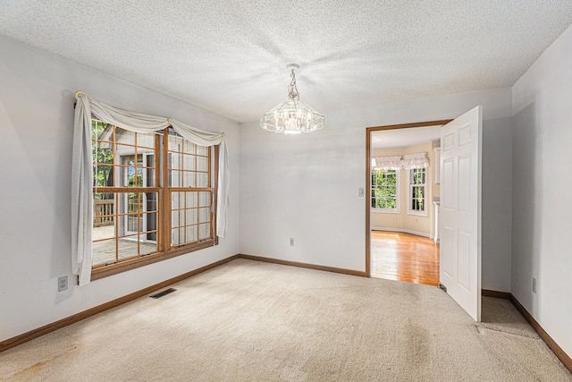 empty room with carpet flooring, an inviting chandelier, and a textured ceiling