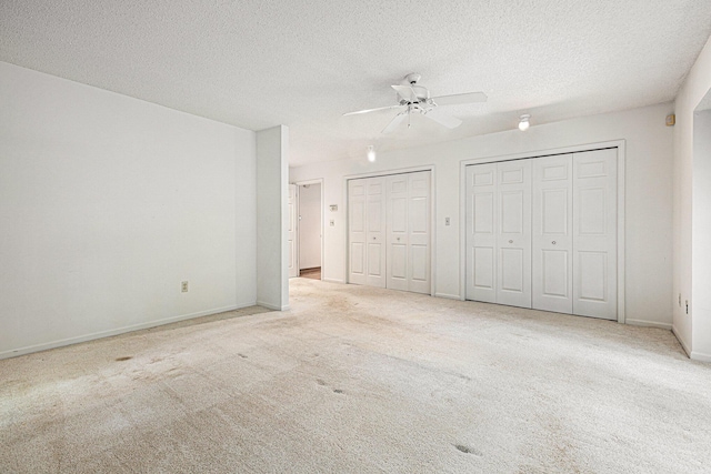 unfurnished bedroom featuring multiple closets, light carpet, a textured ceiling, and ceiling fan