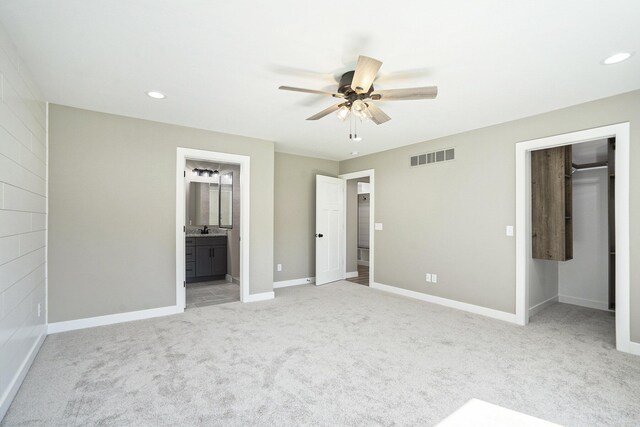 unfurnished bedroom featuring light carpet, connected bathroom, a closet, and ceiling fan