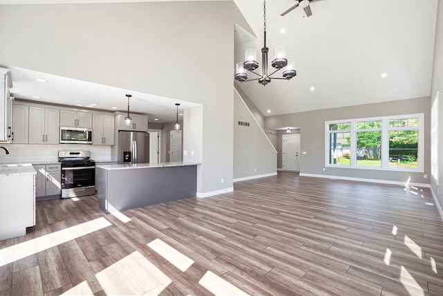 kitchen featuring light wood-type flooring, stainless steel appliances, decorative backsplash, pendant lighting, and high vaulted ceiling