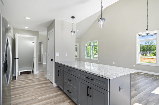 kitchen with gray cabinetry, light stone counters, stainless steel fridge with ice dispenser, light wood finished floors, and baseboards