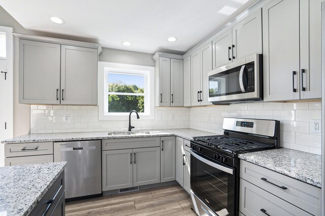 kitchen featuring light hardwood / wood-style floors, appliances with stainless steel finishes, tasteful backsplash, and light stone counters