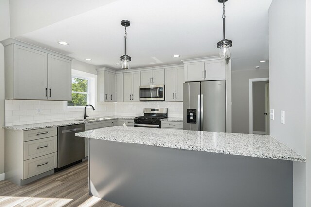 kitchen with tasteful backsplash, stainless steel appliances, light stone counters, hanging light fixtures, and light wood-type flooring