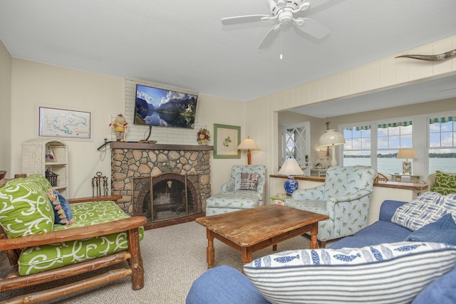 carpeted living room with a stone fireplace, a textured ceiling, and ceiling fan