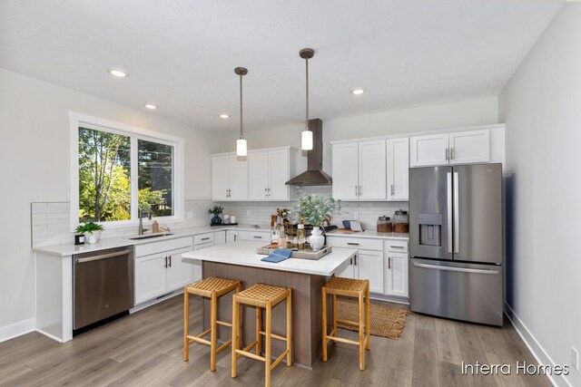 kitchen with white cabinetry, wall chimney range hood, appliances with stainless steel finishes, and light hardwood / wood-style flooring