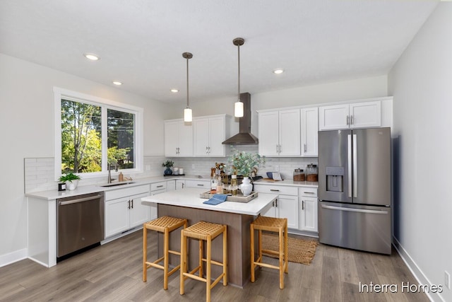 kitchen with a sink, appliances with stainless steel finishes, white cabinets, and wall chimney range hood