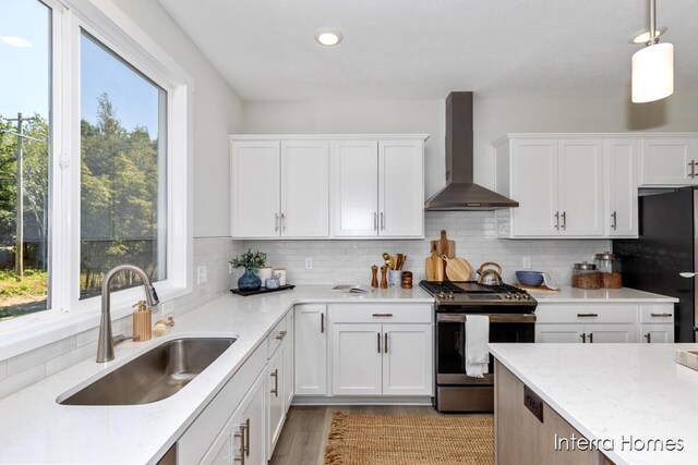 kitchen with freestanding refrigerator, a sink, decorative backsplash, stainless steel gas range oven, and wall chimney range hood