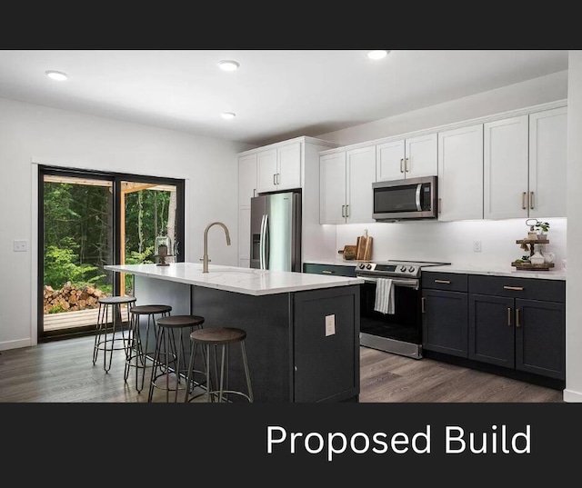 kitchen featuring hardwood / wood-style floors, an island with sink, sink, white cabinets, and stainless steel appliances