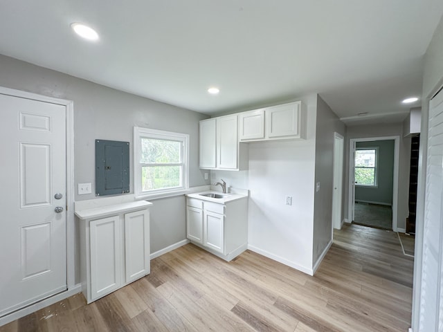 kitchen with white cabinetry, sink, electric panel, and light hardwood / wood-style flooring