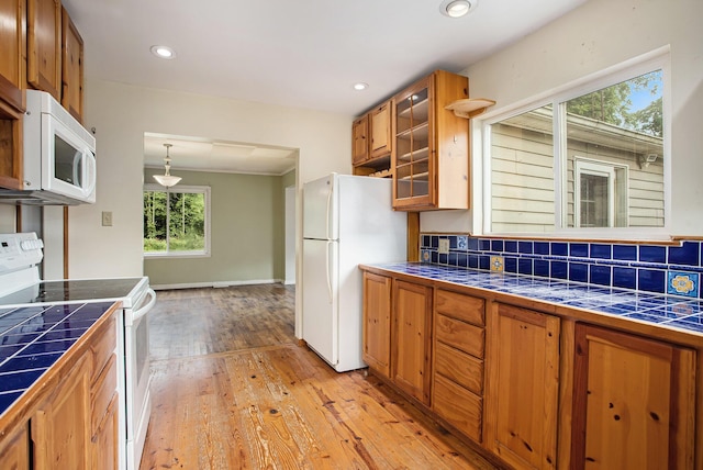 kitchen with tile countertops, backsplash, hanging light fixtures, light hardwood / wood-style floors, and white appliances