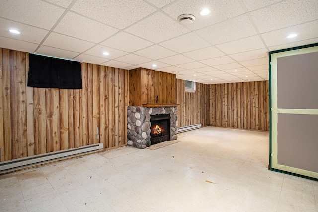 basement with a drop ceiling, a stone fireplace, and baseboard heating