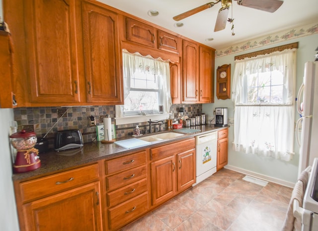 kitchen featuring decorative backsplash, sink, white dishwasher, and dark stone counters