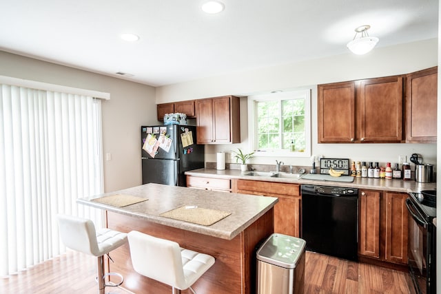 kitchen featuring sink, a kitchen breakfast bar, black appliances, a kitchen island, and light wood-type flooring