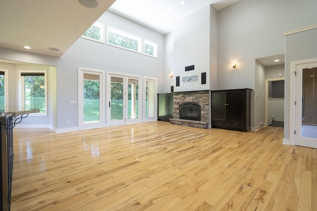 unfurnished living room featuring light hardwood / wood-style floors, a towering ceiling, a fireplace, and a wealth of natural light