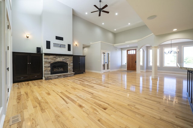 unfurnished living room with a stone fireplace, decorative columns, a towering ceiling, light hardwood / wood-style floors, and ceiling fan with notable chandelier