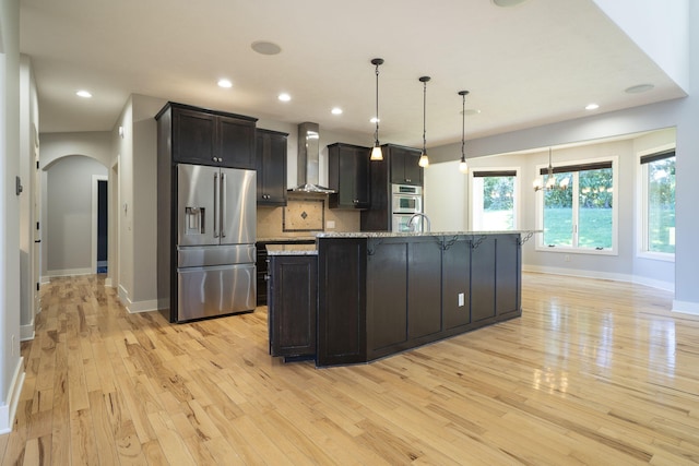 kitchen with light wood-type flooring, wall chimney exhaust hood, stainless steel appliances, pendant lighting, and a large island