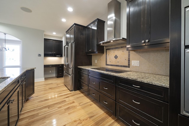 kitchen featuring wall chimney exhaust hood, light stone counters, pendant lighting, light hardwood / wood-style floors, and black electric stovetop