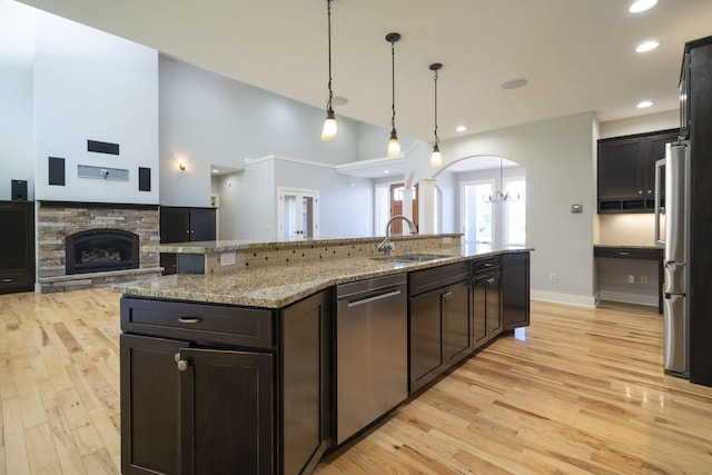 kitchen with appliances with stainless steel finishes, a kitchen island with sink, sink, pendant lighting, and a fireplace