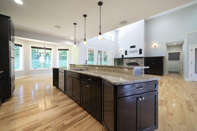 kitchen with sink, a stone fireplace, a large island with sink, light hardwood / wood-style floors, and decorative light fixtures